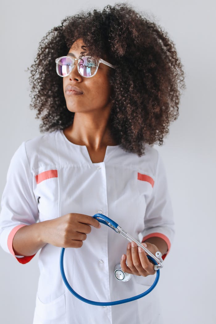 Portrait of a female doctor with curly hair and glasses holding a stethoscope in a medical setting.