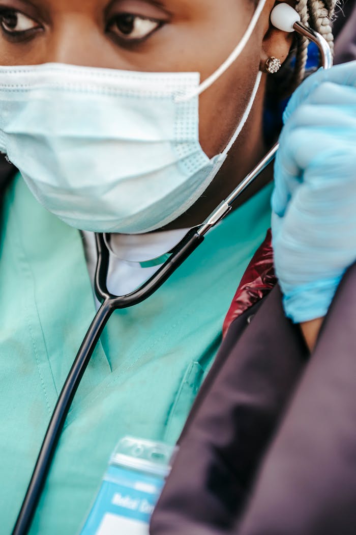 Crop African American female doctor in medical mask and uniform putting on stethoscope and looking away